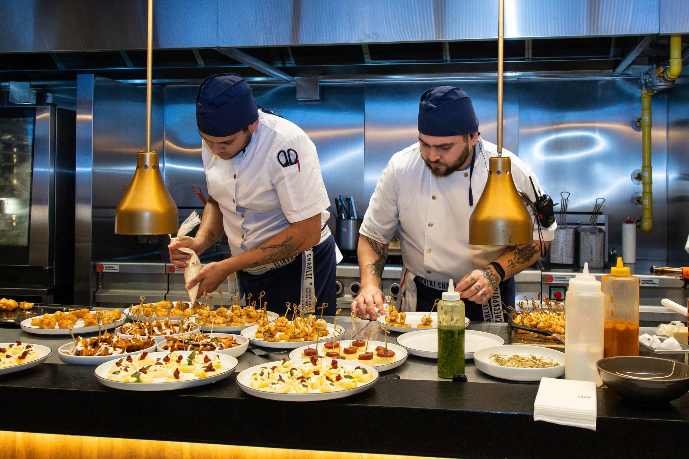 Dos cocineros armando bandejas de bocados en la cocina abierta
