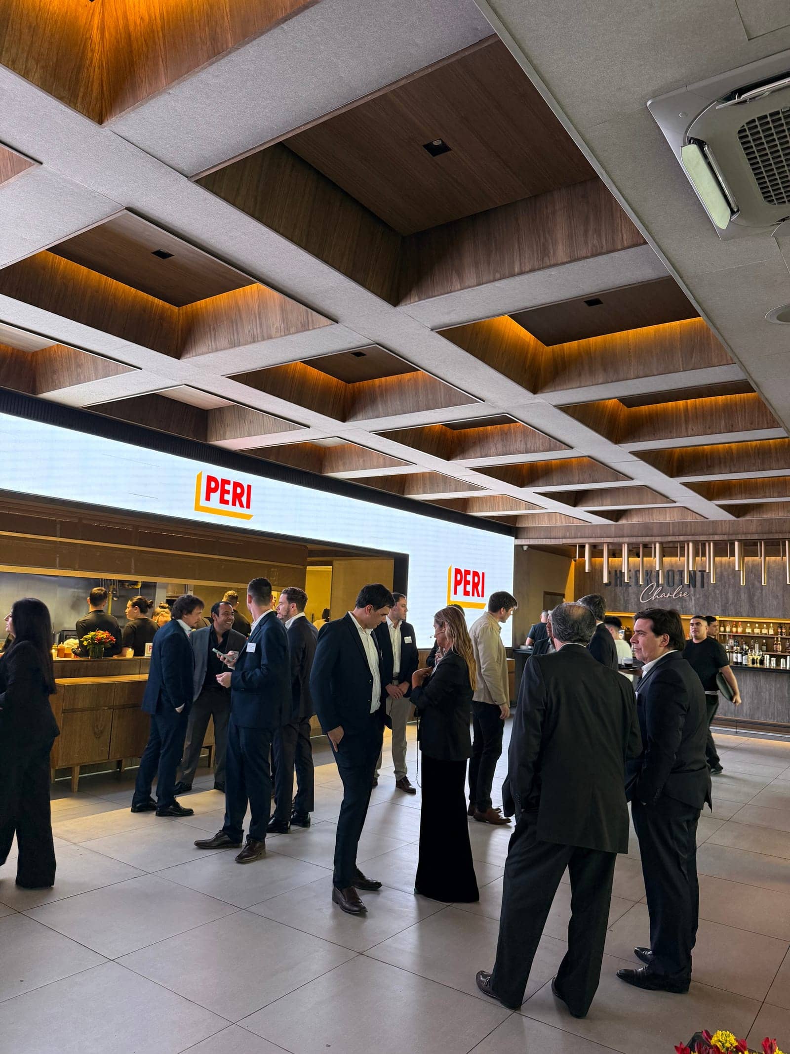 Evento corporativo en el salón, con invitados de traje frente a la pantalla LED con la marca del cliente