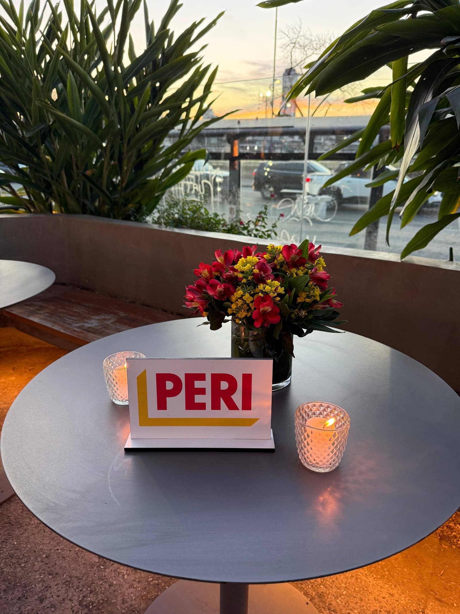 Mesa alta en la terraza al atardecer, con flores, velas y el cartel del evento