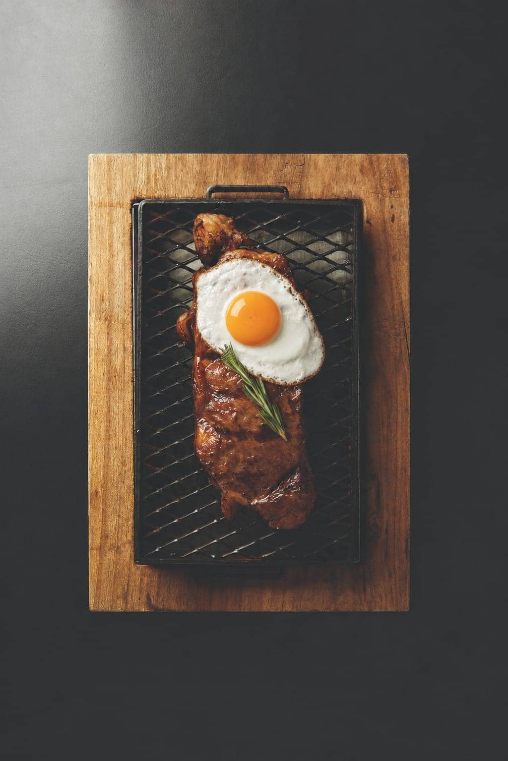 Bife de chorizo a caballo con huevo frito y romero, sobre parrilla de hierro