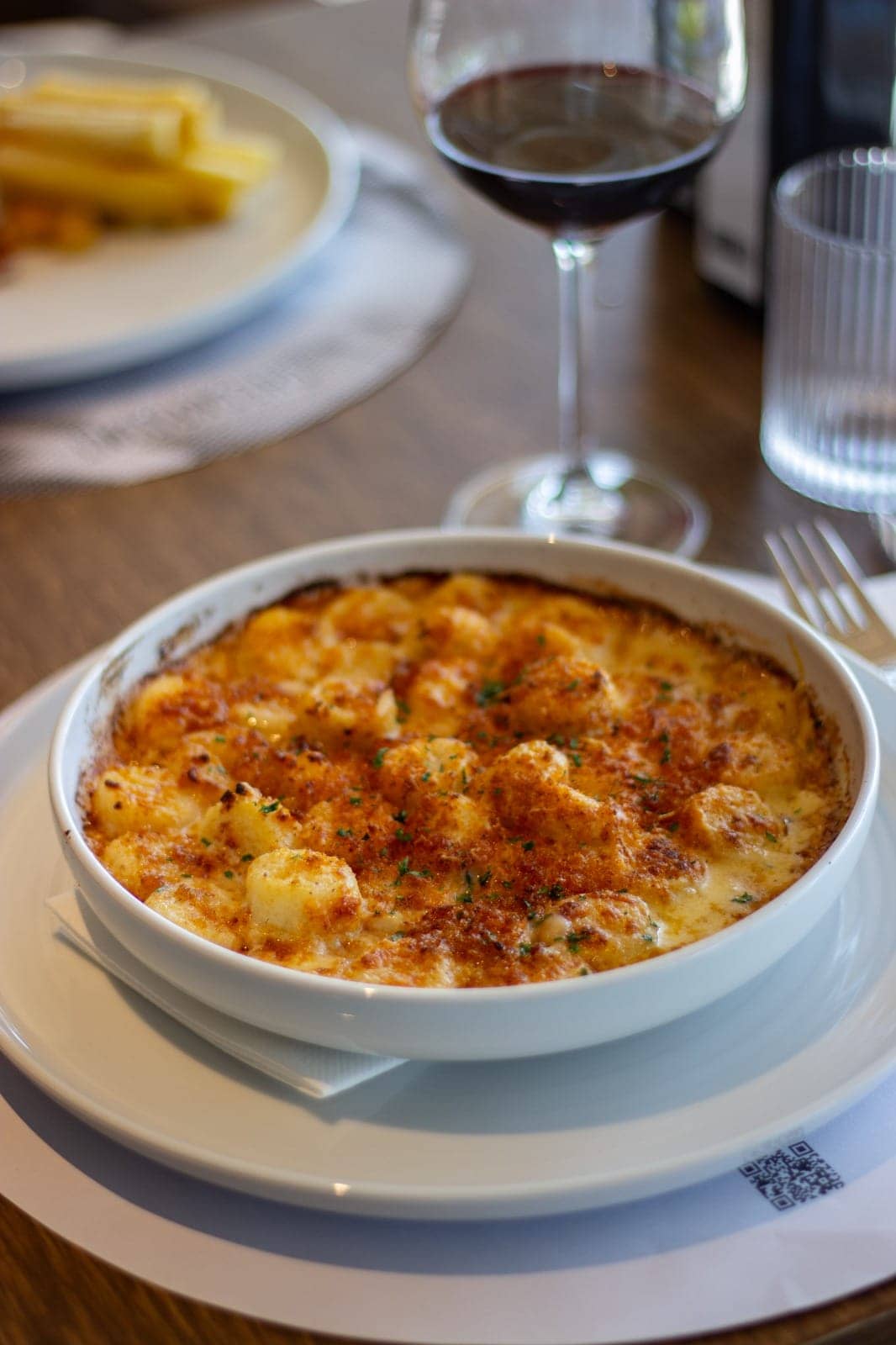 Gnocchi soufflé gratinados en fuente, junto a una copa de vino tinto