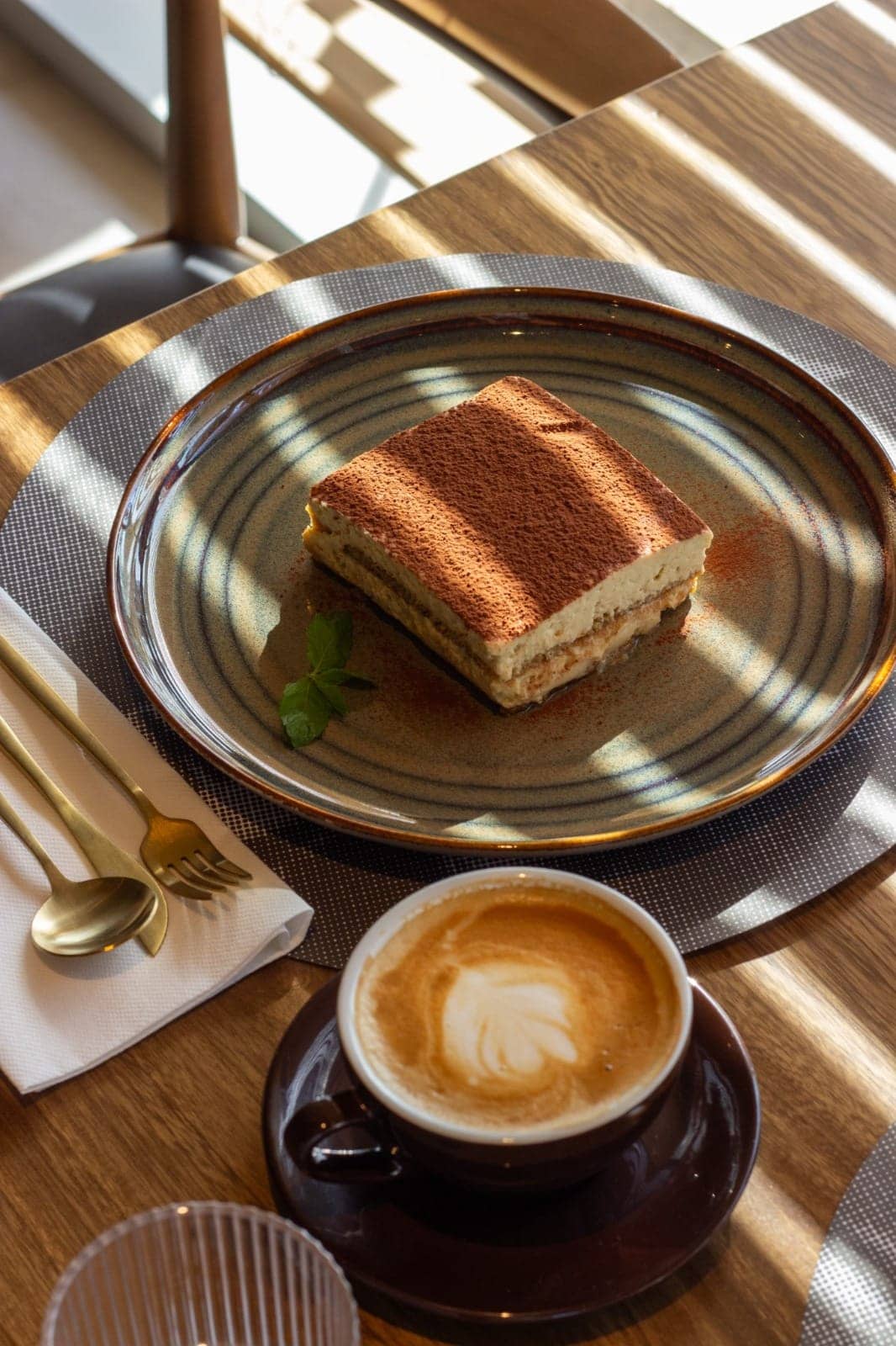 Tiramisú y un café con leche servidos en una mesa al sol
